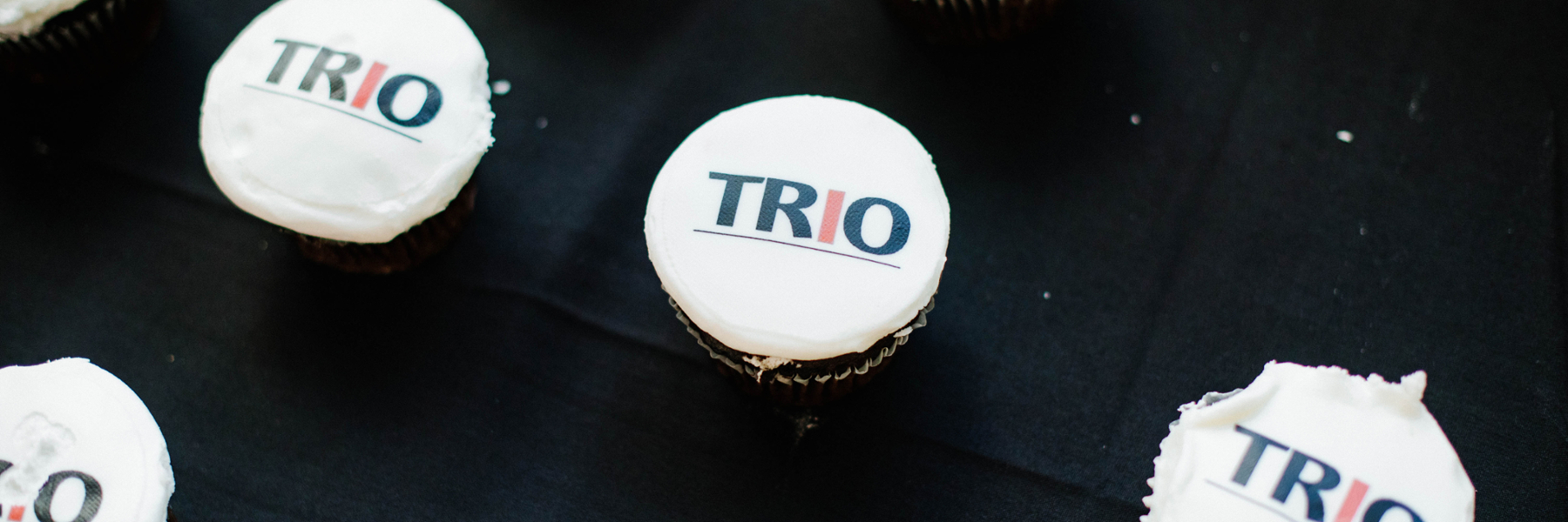 Cupcakes on a table with the TRIO logo on the icing.