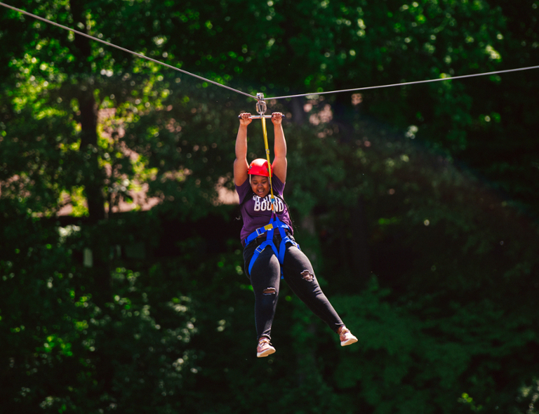 An female Upward Bound student ziplining in a forest.